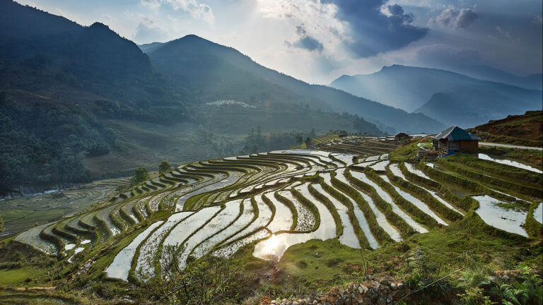 Mirror-like rice terraces in Northern Vietnam during pouring water season with farmers planting rice.